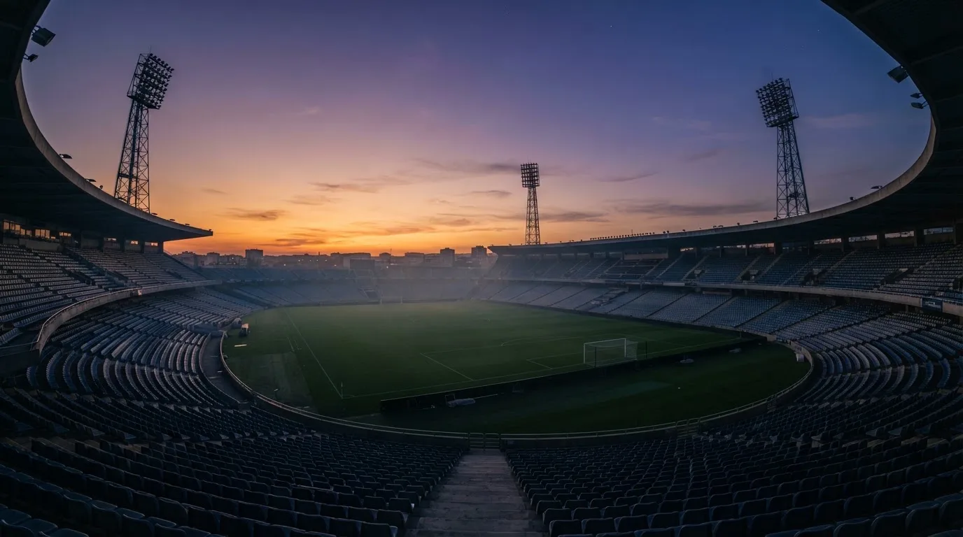 An empty football stadium with floodlight masts at dusk