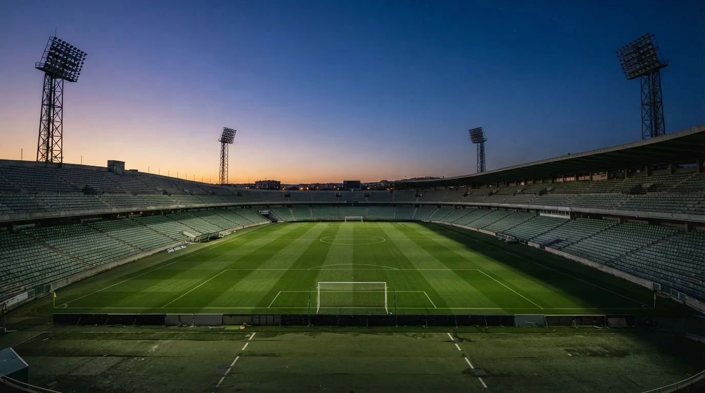 An empty football stadium with floodlight masts at dusk