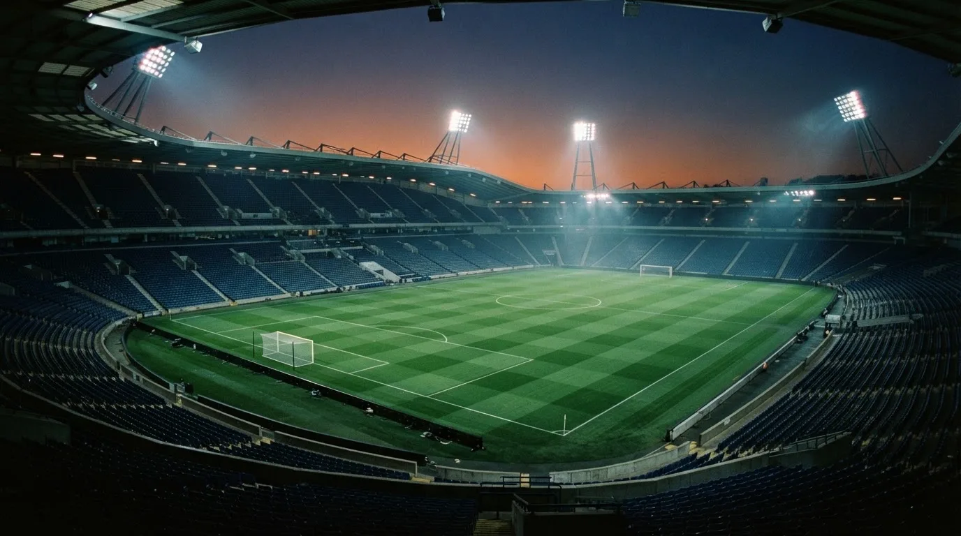 An empty football stadium with floodlight masts at dusk
