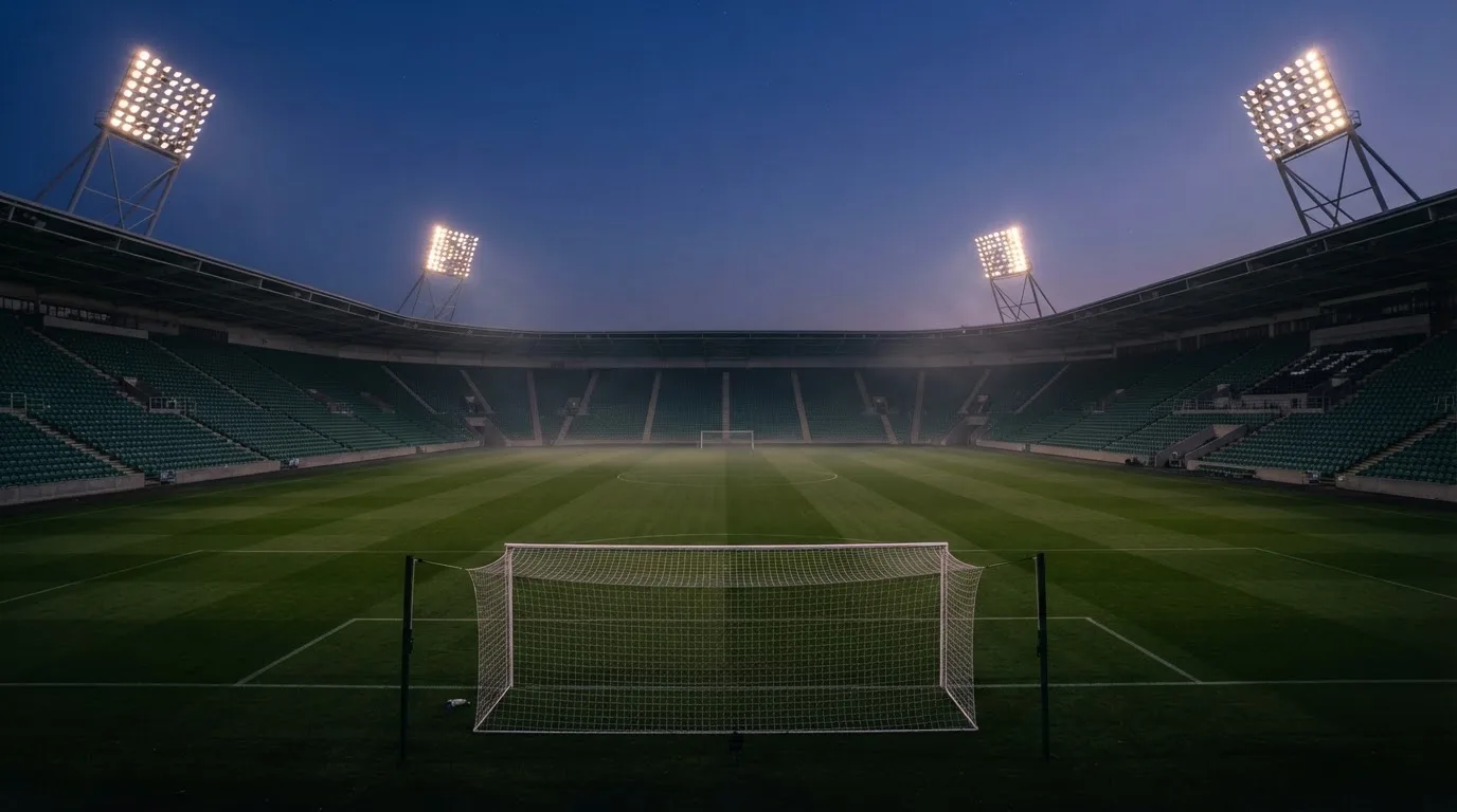 An empty football stadium with floodlight masts at dusk
