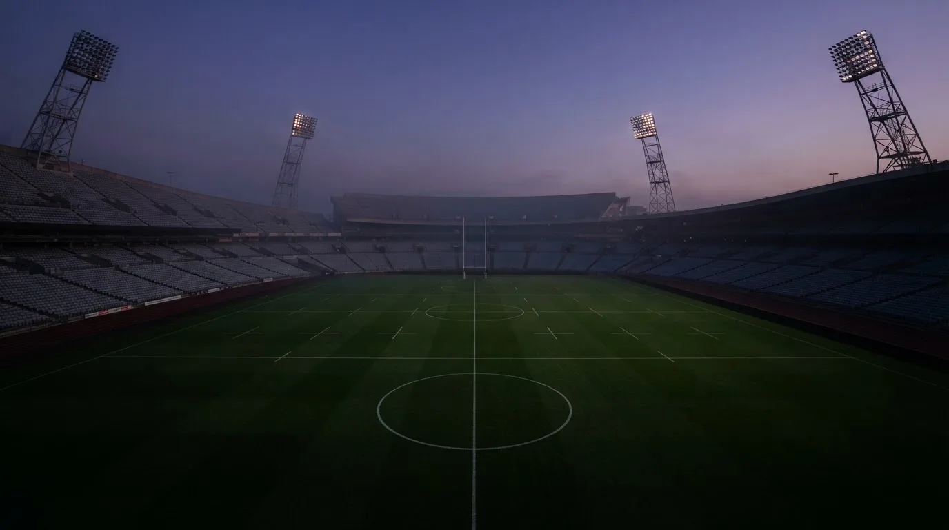 An empty football stadium with floodlight masts at dusk