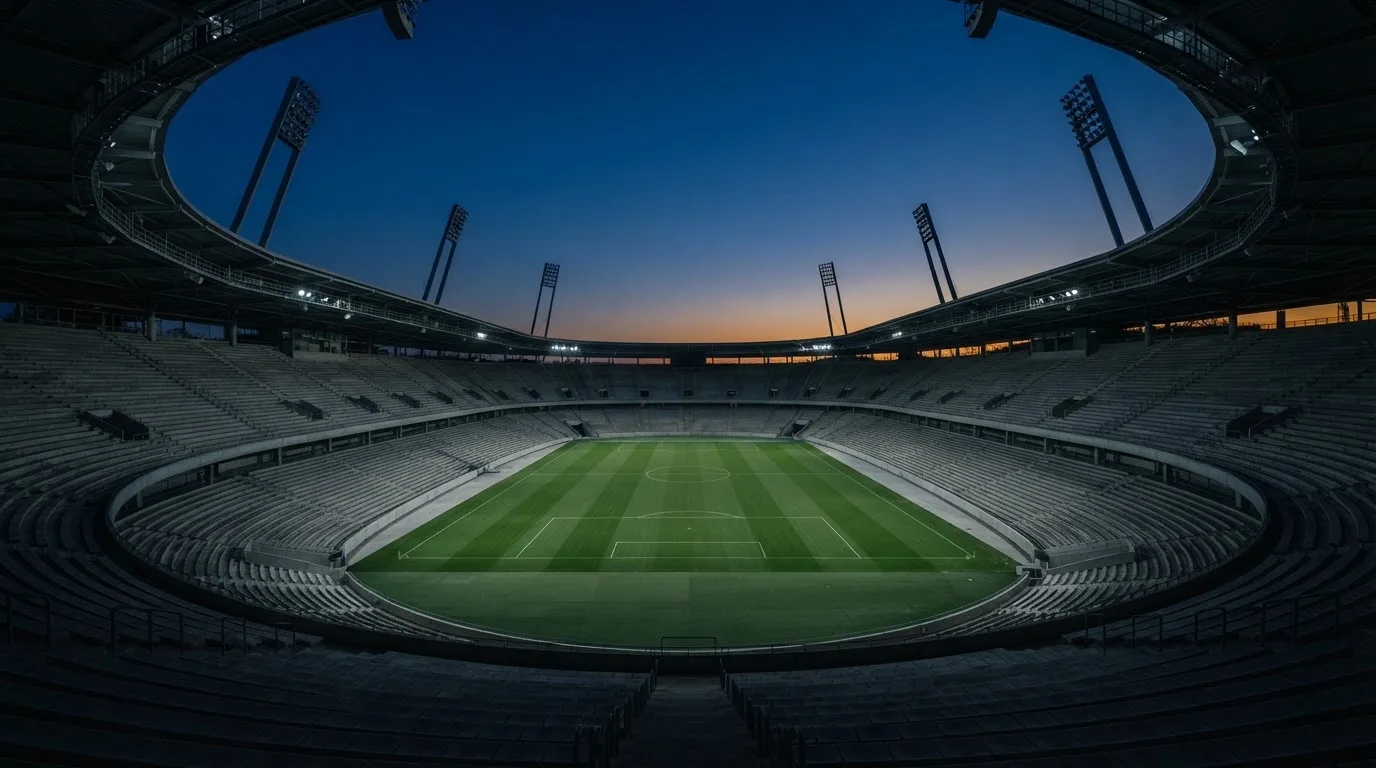 An empty football stadium with floodlight masts at dusk